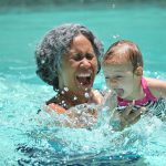 grandmother splashing in a pool with grandchild.