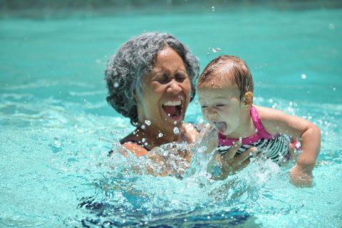 grandmother splashing in a pool with grandchild.