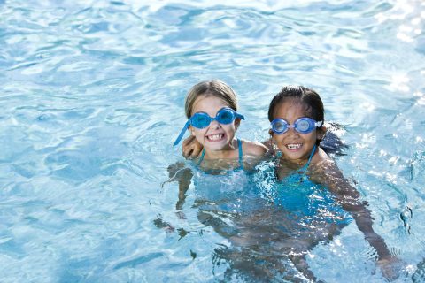 Two girls wearing swim goggles playing together in swimming pool.