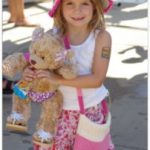 girl in a pink and white dress holding a bear.