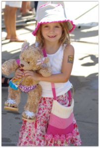 girl in a pink and white dress holding a bear.