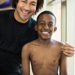 closeup of a man with his arm around a kid and both are smiling.