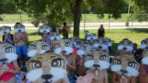 a group of kids outside holding otter masks on their faces.