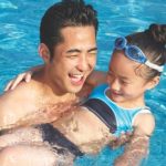 a father holding his daughter and helping her float in the pool.