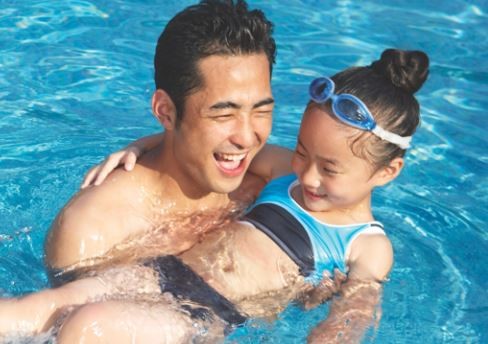 a father holding his daughter and helping her float in the pool.