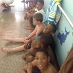 a group of boys at a pool sitting against a wall.