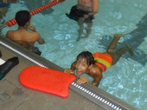 a girl holding on the side of a pool looking up at the camera.