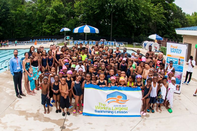 A group of kids in front of a sign stating "the worlds largest swimming lesson"