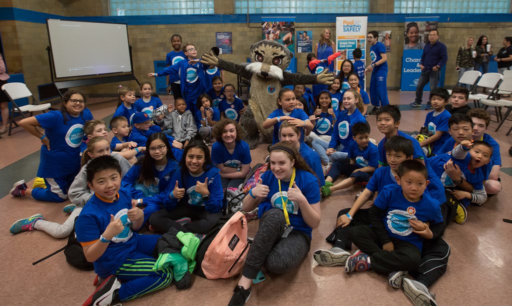 a group of kids in blue shirts posing with a person in an otter costume.