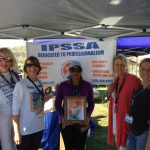 group of women standing in front of an i.p.s.s.a banner with a photograph of a young boy.