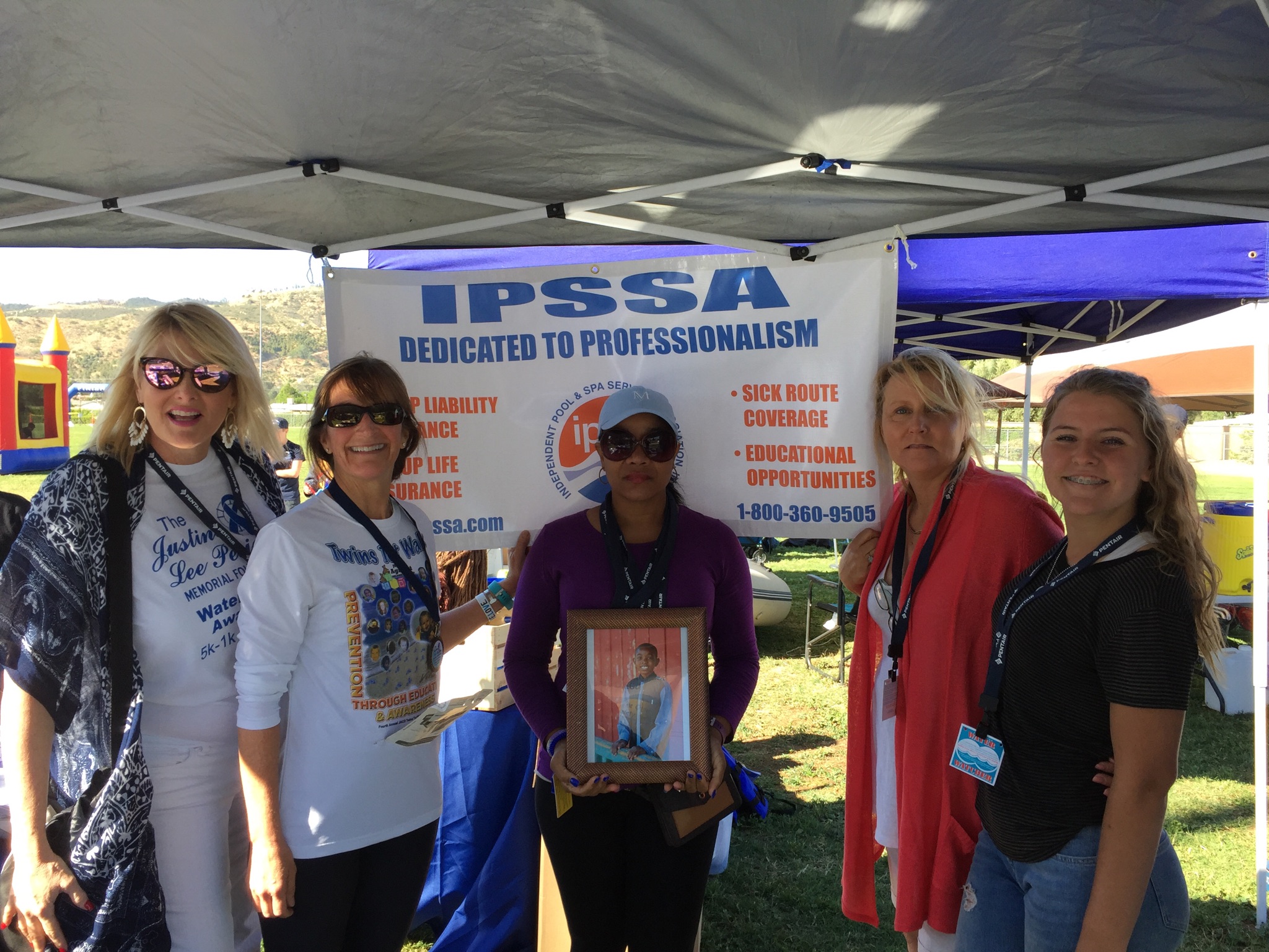 group of women standing in front of an i.p.s.s.a banner with a photograph of a young boy.