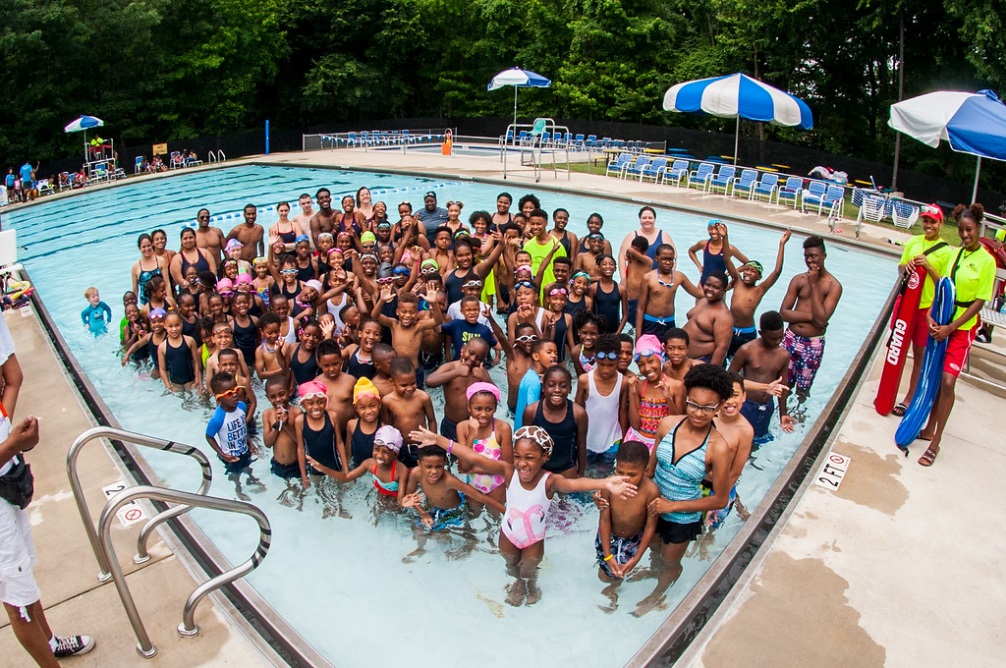 a large group of children and adults in a pool smiling and posing for the camera.