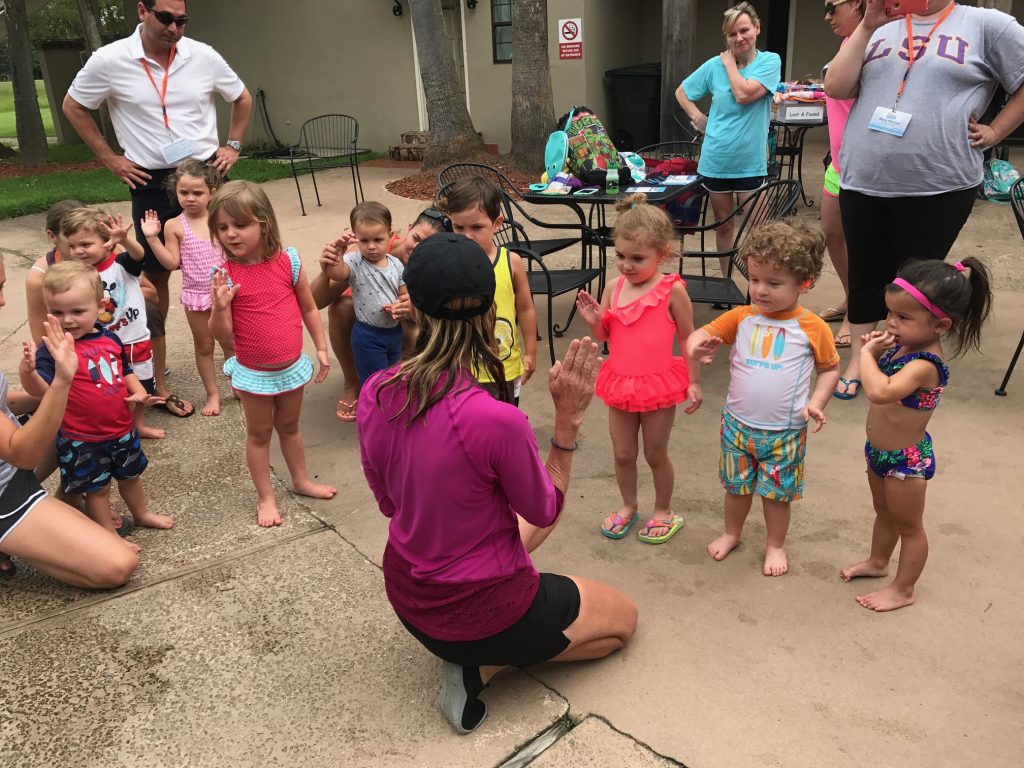 a group of very young children standing around a woman crouched down with her hand raised.