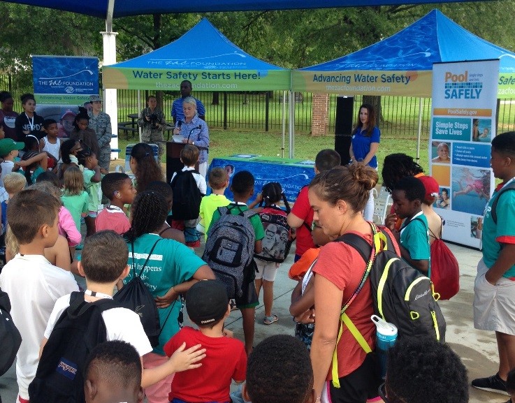 woman speaking to a group of children outside.