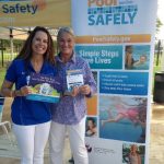 two women smiling and standing in front of a pool safely sign.