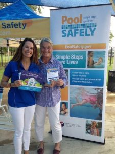 two women smiling and standing in front of a pool safely sign.