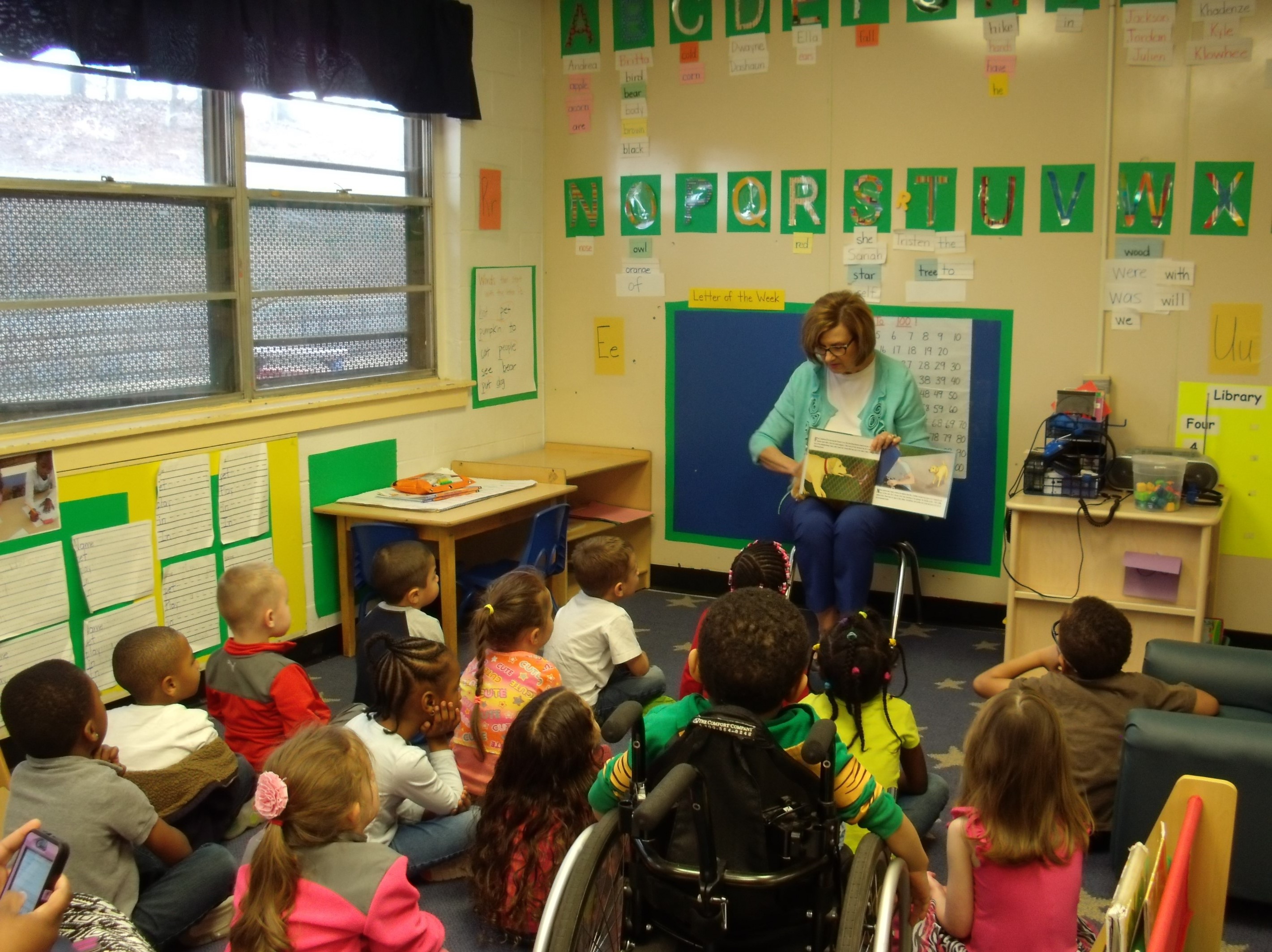 children sitting listening to a woman reading a book.