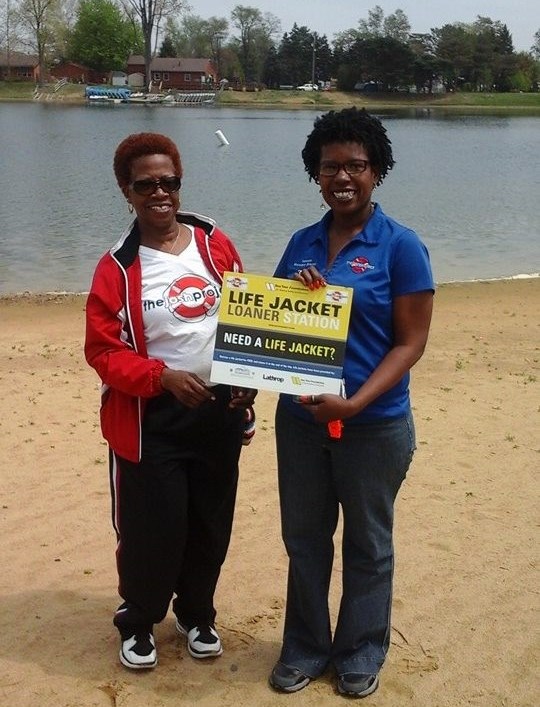 two women standing in front of a lake with a sign.