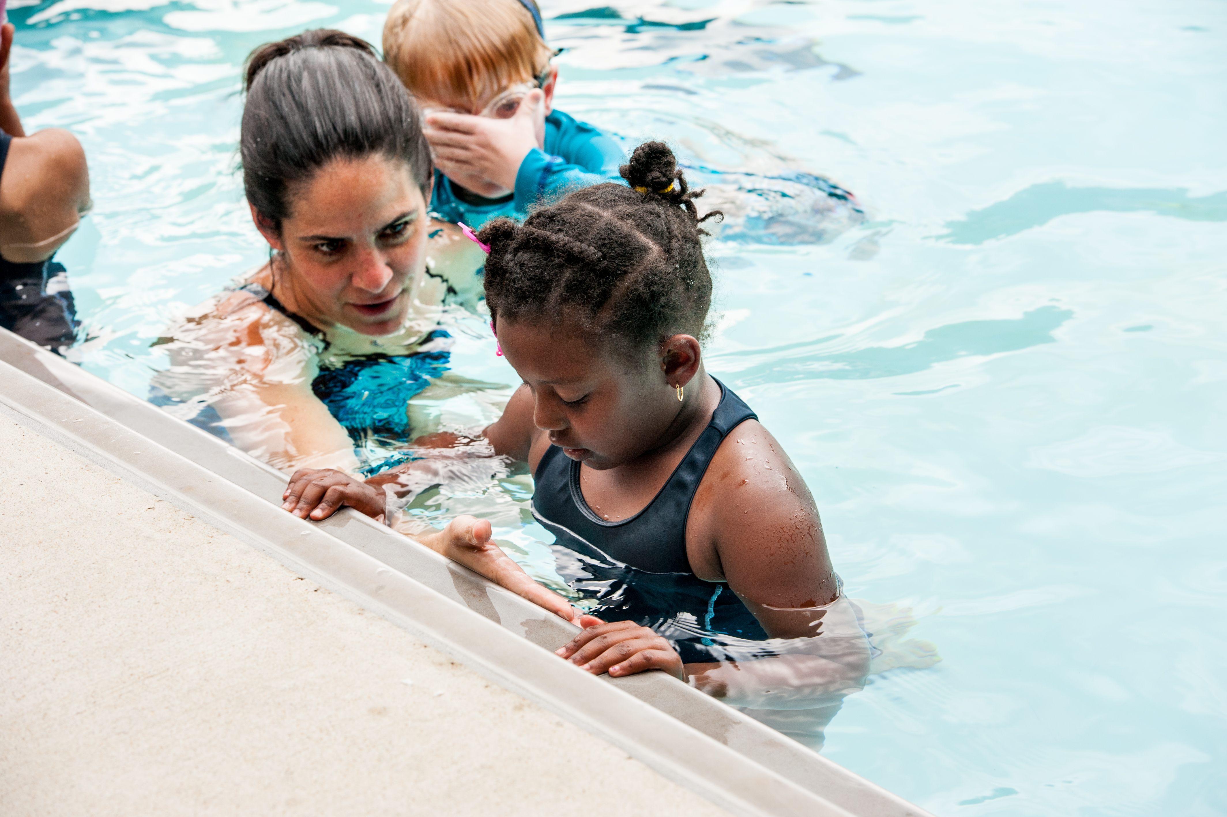 an adult woman talking to a child who is holding onto the side of the pool.