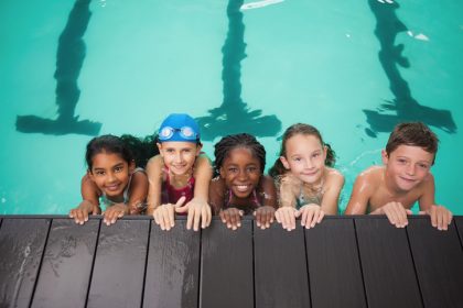 five smiling kids in a pool at the edge