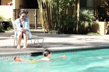 a woman watching a kid swim in a pool