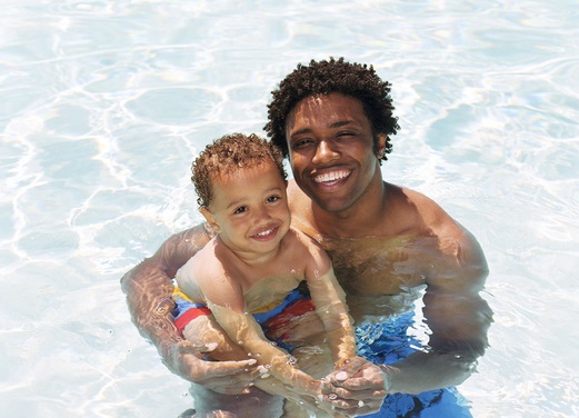 Father and son (2-4) in swimming pool, smiling, portrait.
