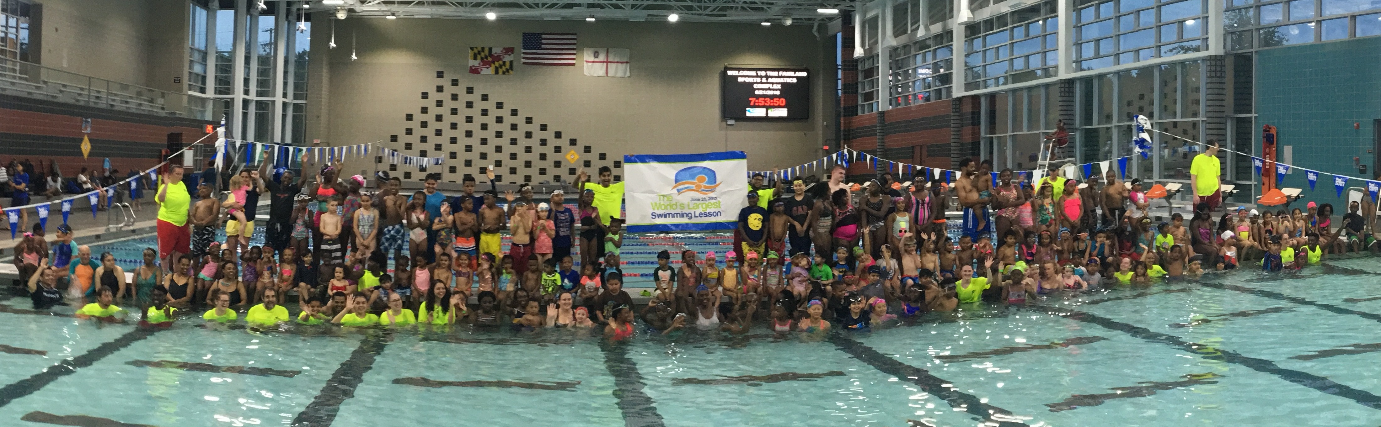 a large group of children sitting and standing around the edge of a large pool.