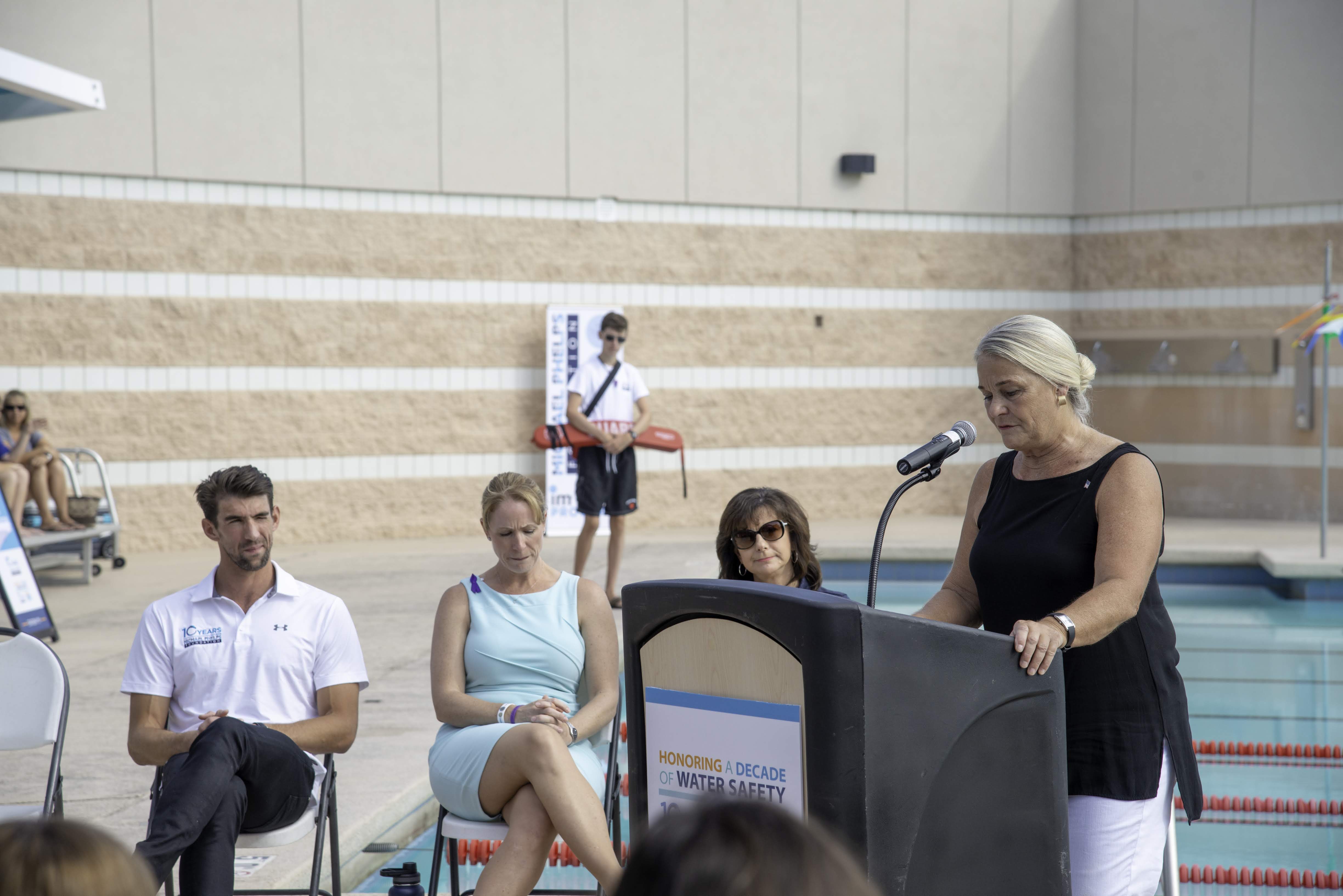 woman standing at a podium with a pool in the background.