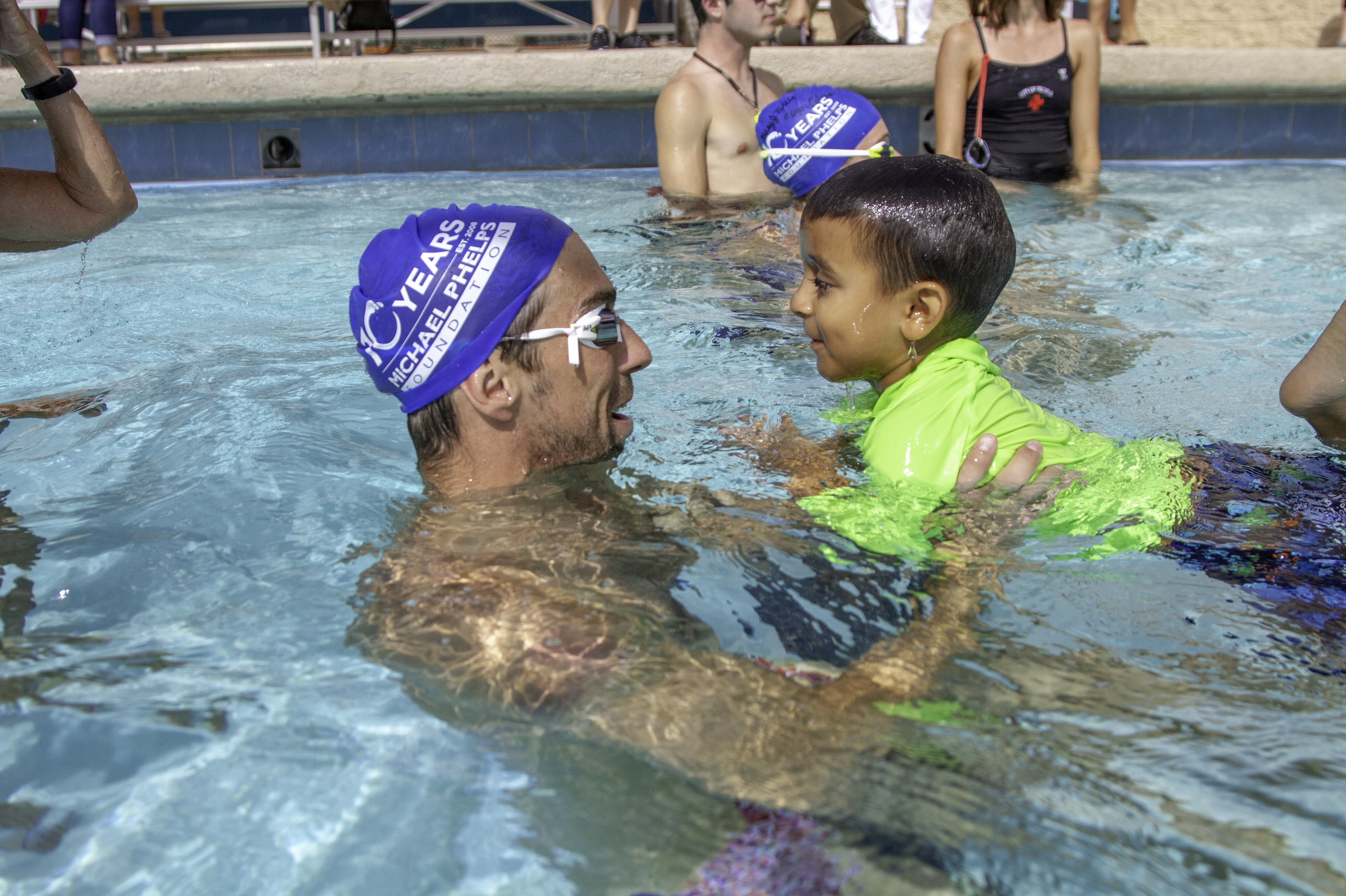 michael phelps in a pool helping a young child to swim.