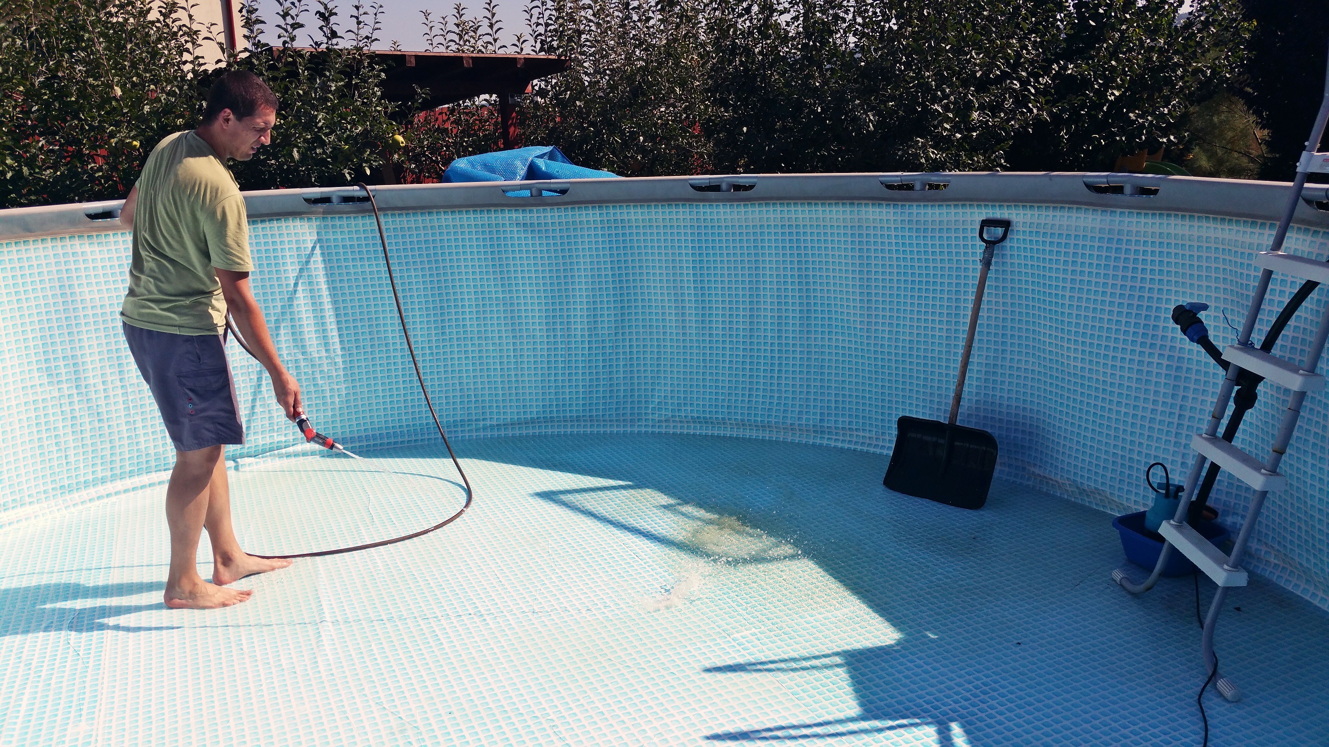 Horizontal image of a 40 years old man cleaning the backyard pool with water from a hose.
