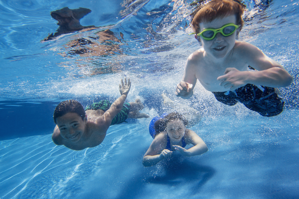 Three children swimming underwater, smiling at the camera.