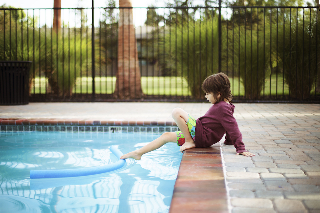 Boy playing with noodle float while sitting poolside