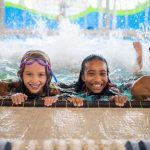 four kids in a pool holding on to the edge and kicking