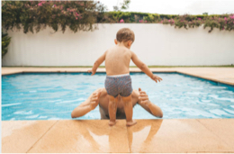 a child on the side of a pool ready to jump into a man's arms.