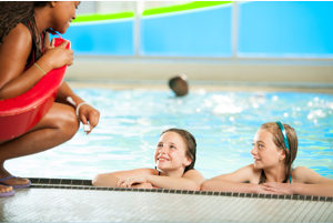 two kids in a pool looking up at an instructor.