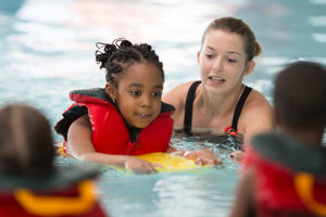 a child wearing a life vest with an adult in a pool.