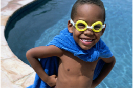 a young boy with goggles and a towel around his neck like a cape.