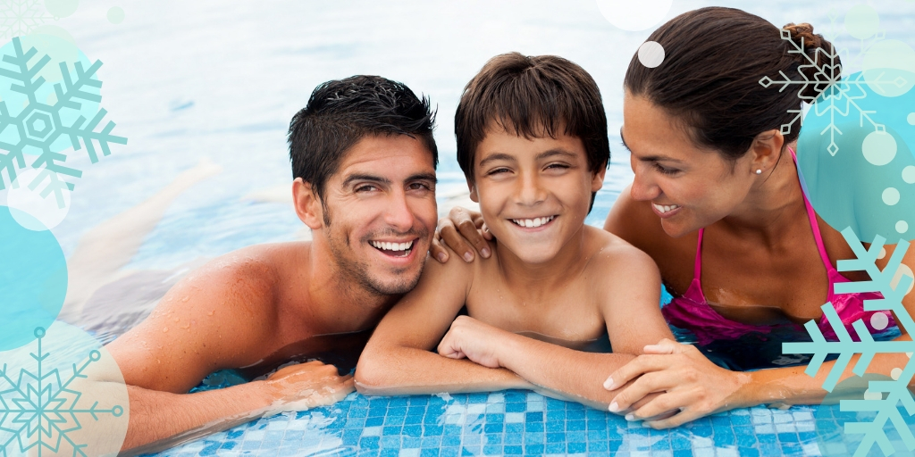 a mother and father with their child smiling by the edge of a pool.