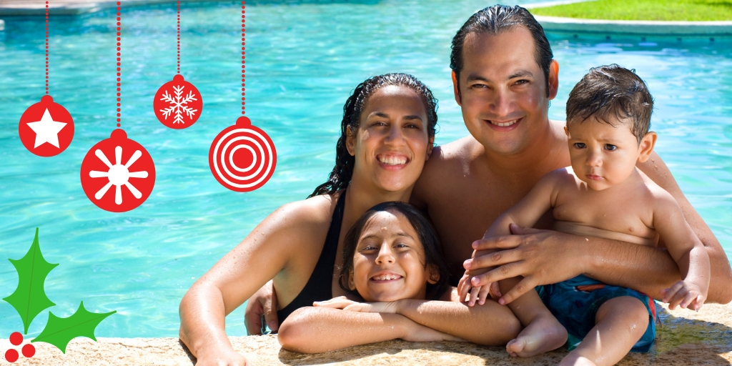 a mother father and two children smiling by the edge of a pool.