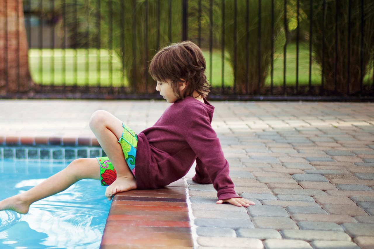 A child sitting by the edge of a pool dipping one foot in.