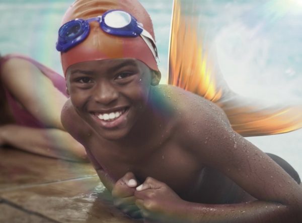 a young boy resting on the edge of a pool with gold fins coming from his back.