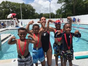 4 kids and 1 adult flexing their muscles standing in front of a pool