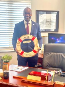 a smiling man standing behind a desk holding a flotation device