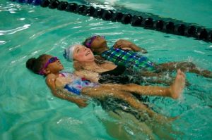 a woman floats on her back while holding two children who are also on their backs.